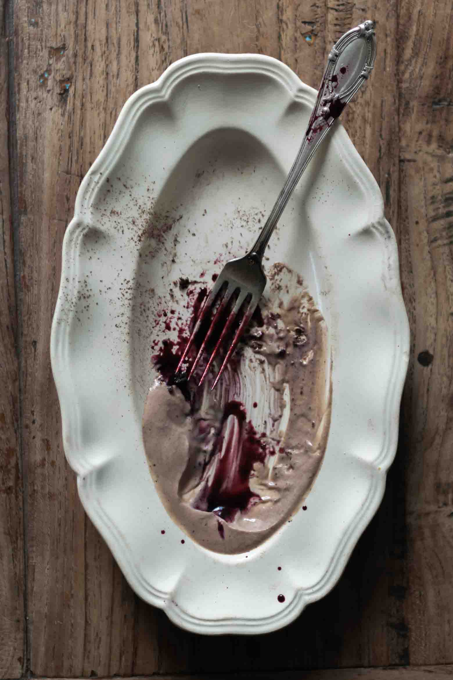 Chocolate mousse and black currant-rosemary syrup remnants on a plate with a fork.